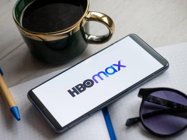 Ein Smartphone mit dem HBO-Max-Schriftzuf auf dem Display liegt auf einem Tisch.