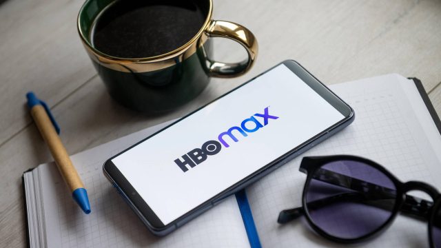 Ein Smartphone mit dem HBO-Max-Schriftzuf auf dem Display liegt auf einem Tisch.