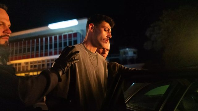 Koder Alian in Asbest: Polizei führt nachts einen jungen Mann in Handschellen zu einem Auto.