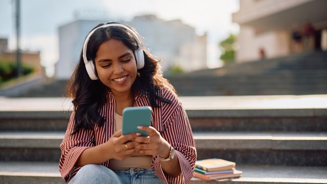 Auf dem Bild in dem Artikel zu den besten Hörbüchern 2025 laut BookBeat ist eine junge Frau mit langen dunklen Haaren mit Kopfhörern zu sehen.