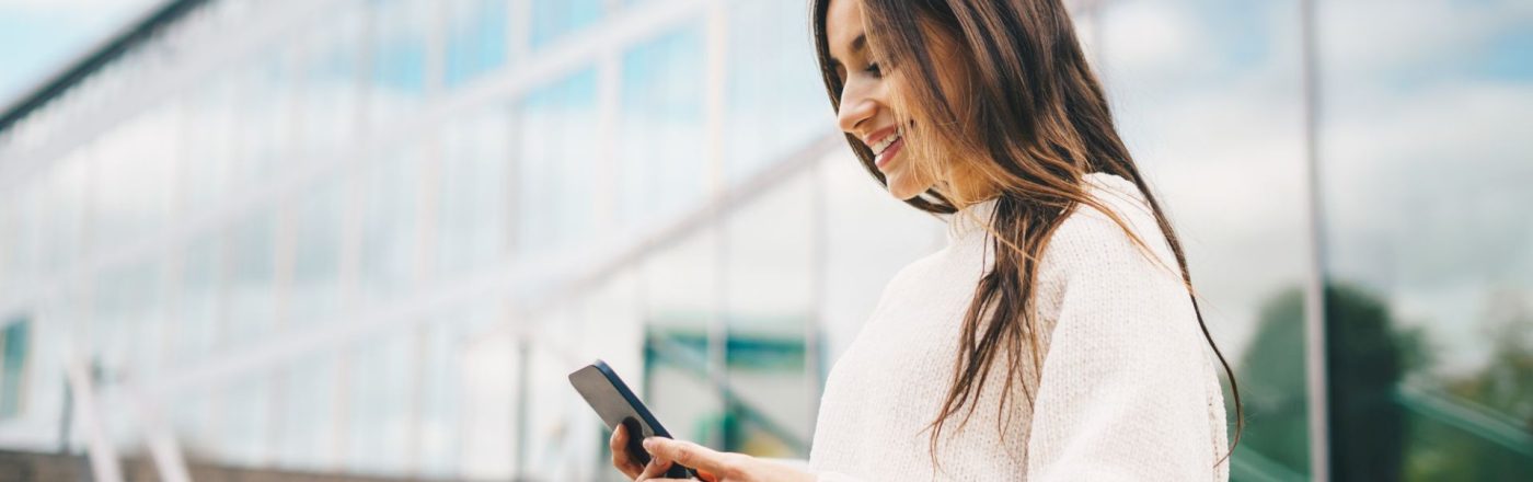 Junge Frau schaut auf ein Handy, das sie in den Händen hält.