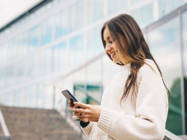 Junge Frau schaut auf ein Handy, das sie in den Händen hält.