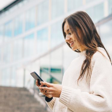 Junge Frau schaut auf ein Handy, das sie in den Händen hält.