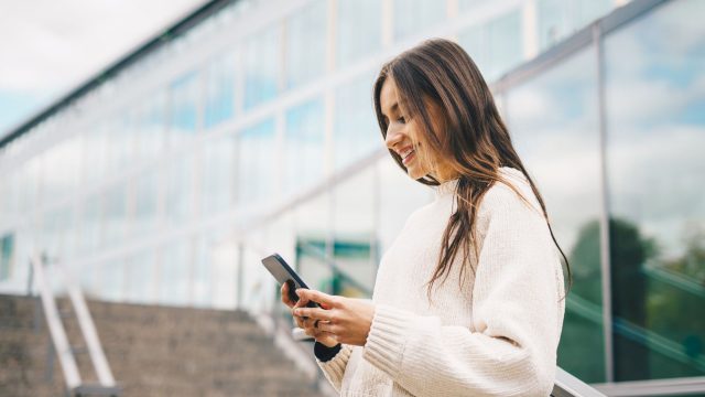Junge Frau schaut auf ein Handy, das sie in den Händen hält.