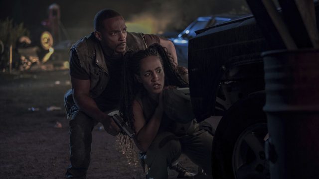 Anthony Mackie und Tiana Okoye hocken in einer "Twisted Metal"-Szene hinter einem Auto.
