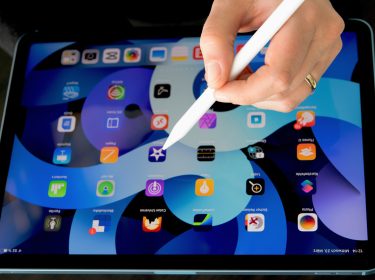 Weibliche Hand mit Apple Pencil über dem iPad Air 2022, auf dem der Startbildschirm zu sehen ist