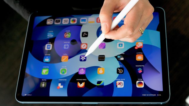 Weibliche Hand mit Apple Pencil über dem iPad Air 2022, auf dem der Startbildschirm zu sehen ist