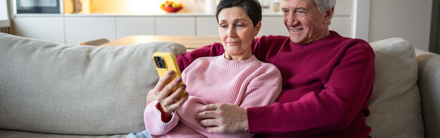 Ein älteres Pärchen sitzt auf dem Sofa und schaut auf ein Smartphone.