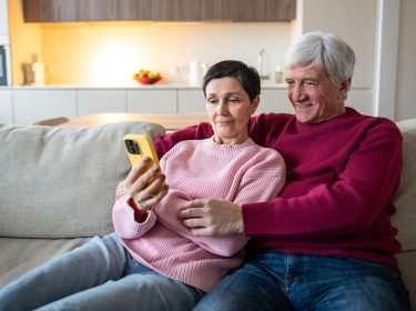 Ein älteres Pärchen sitzt auf dem Sofa und schaut auf ein Smartphone.