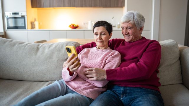 Ein älteres Pärchen sitzt auf dem Sofa und schaut auf ein Smartphone.