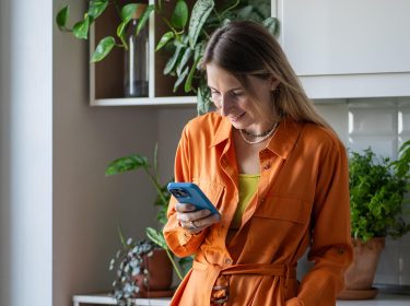 Eine Frau lehnt an einem Schrank und schaut auf ein Smartphone.