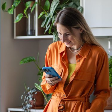 Eine Frau lehnt an einem Schrank und schaut auf ein Smartphone.