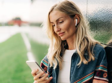 Eine Frau schaut auf ein Smartphone und nutzt AirPods.