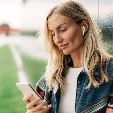 Eine Frau schaut auf ein Smartphone und nutzt AirPods.