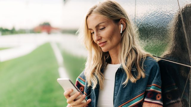 Eine Frau schaut auf ein Smartphone und nutzt AirPods.