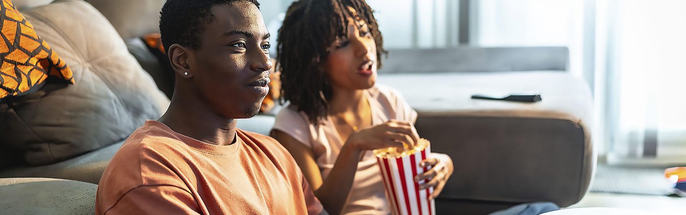 Ein junges Paar sitzt vor dem Sofa auf dem Boden und schaut Fernsehen.