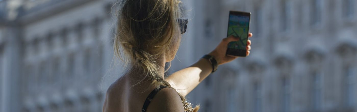 Eine junge Frau hält ihr Handy hoch, während sie vor dem Buckingham Palast in London 