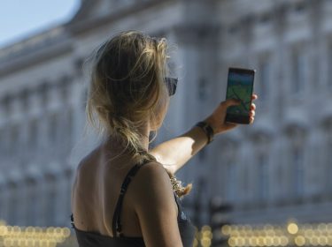 Eine junge Frau hält ihr Handy hoch, während sie vor dem Buckingham Palast in London 