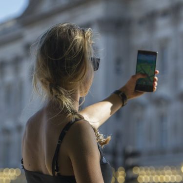 Eine junge Frau hält ihr Handy hoch, während sie vor dem Buckingham Palast in London 