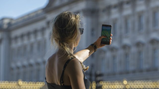 Eine junge Frau hält ihr Handy hoch, während sie vor dem Buckingham Palast in London "Pokémon GO" spielt.