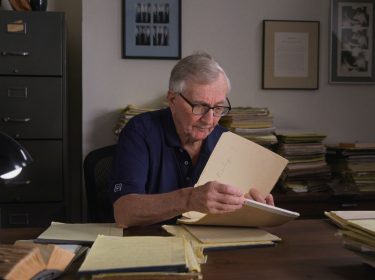 Seymour Hersh sitzt an einem Schreibtisch und blättert durch seine Unterlagen.