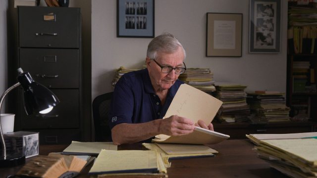 Seymour Hersh sitzt an einem Schreibtisch und blättert durch seine Unterlagen.