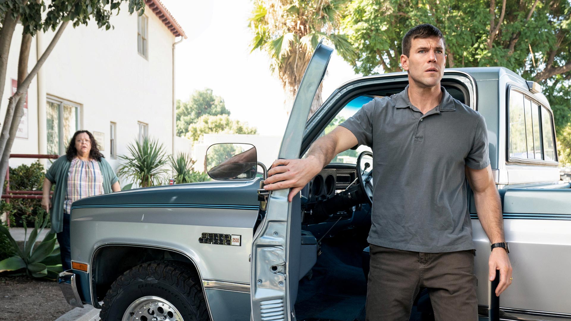 Auf dem Bild in den GigaTV-Highlights im Januar 2026 siehst du eine Szene aus Navy CIS: Origins. Austin Stowell als Leroy Jethro Gibbs steht mit ernster Miene neben einem silbernen Pickup-Truck und hält die Fahrertür offen.