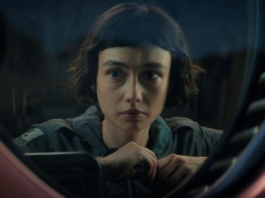 In den besten Serien 2025 siehst du eine Szene aus Alien: Earth. Sydney Chandler als Wendy blickt ernst und konzentriert durch ein rundes Fenster mit technischer Umrahmung.