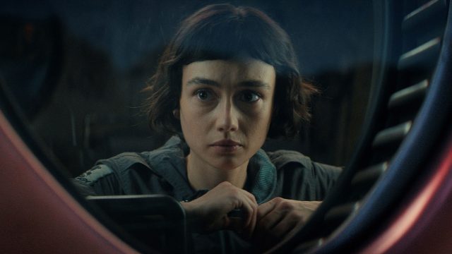 In den besten Serien 2025 siehst du eine Szene aus Alien: Earth. Sydney Chandler als Wendy blickt ernst und konzentriert durch ein rundes Fenster mit technischer Umrahmung.
