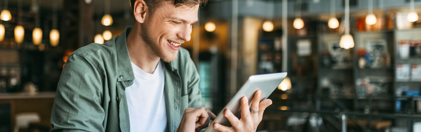 Ein junger Mann sitzt in einer Buchhandlung und schaut auf ein Tablet.