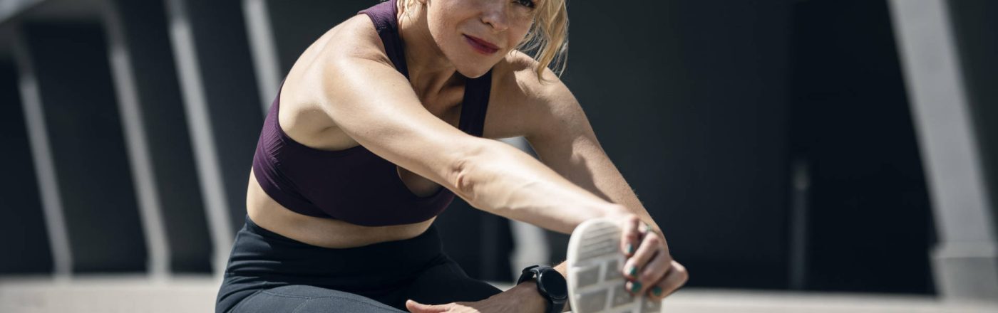 Eine Frau in sportlicher Kleidung sitzt auf dem Boden und dehnt sich.