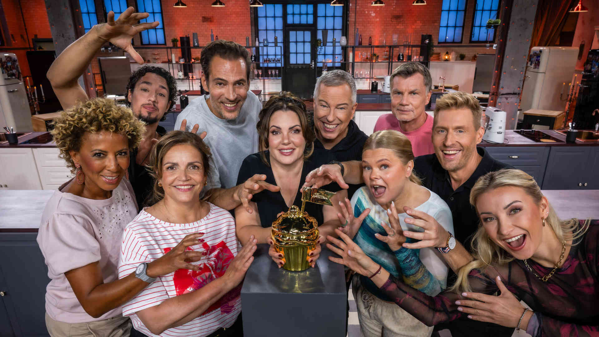 Die Teilnehmer der 10. Staffel "Promibacken" stehen rund um die goldene Sieger-Trophäe.