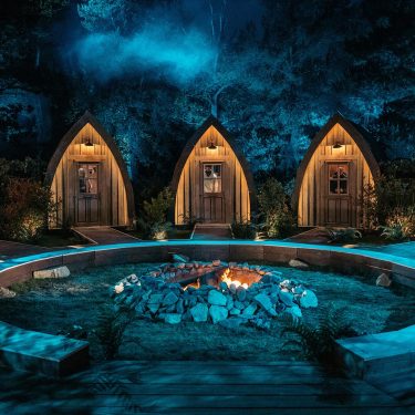 Auf dem Bild in dem Artikel zu „Werwölfe“ Staffel 2 ist ein nächtliches Set mit fünf kleinen, beleuchteten Holzhütten zu sehen.