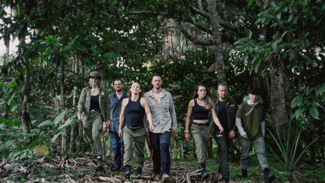 Auf dem Bild zu 7 vs. Wild Gewinner:innen sind sieben Teilnehmende im Dschungel zu sehen. Von links nach rechts: Jeannine Michaelsen, Joe Vogel, Fibii, Lucas „Avive“ Michels, Imke Salander, Kris Grippo und David Leichtle. Alle tragen Outdoor-Kleidung und wirken fokussiert und entschlossen, während sie durch dichtes Grün marschieren.