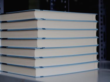 Bücher stehen gestapelt in einem Regal.