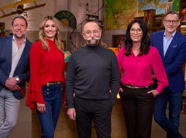 Auf dem Bild mit den Bares für Rares-Expert:innen stehen fünf bekannte Gesichter der Sendung lächelnd nebeneinander im Studio. Von links nach rechts sind Patrick Lessmann, Bianca Berding in roter Bluse, Moderator Horst Lichter mit markantem Schnurrbart, Heide Rezepa-Zabel in pinker Bluse und Detlev Kümmel im blauen Sakko zu sehen. Die Stimmung wirkt freundlich und professionell.