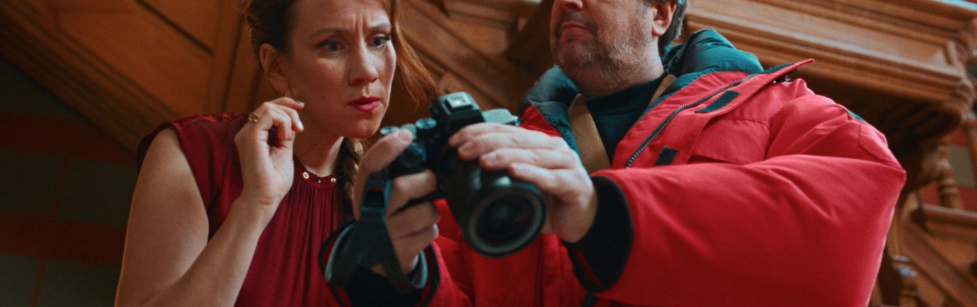 In den Streaming-Highlights im Februar 2026 ist eine Szene aus „Fabian und Die mörderische Hochzeit“ zu sehen. Zu sehen ist Bastian Pastewka, der in einer roten Jacke eine Kamera prüft, während eine Frau neben ihm gespannt hinschaut.