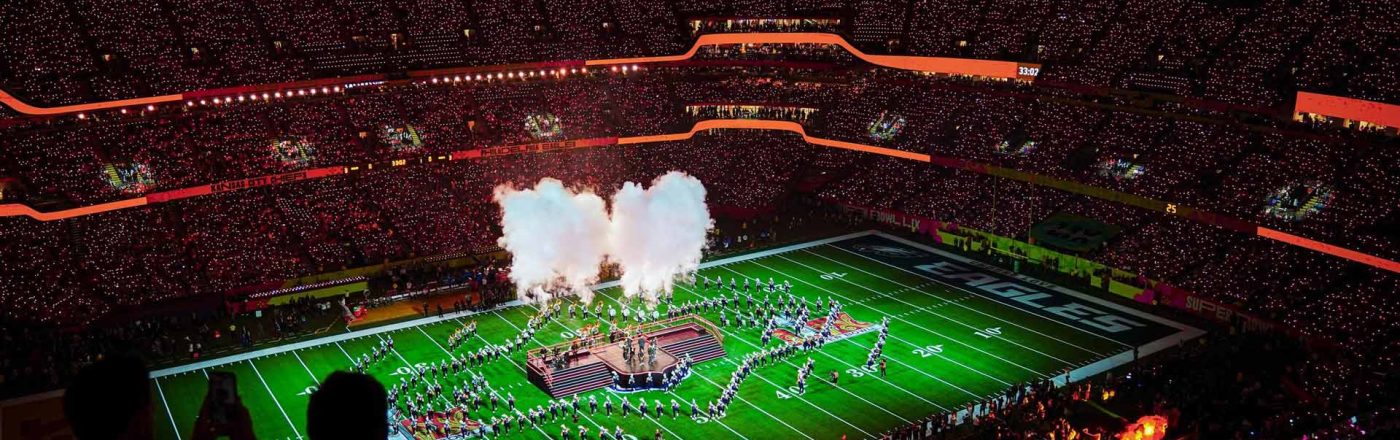 Auf dem Bild in den GigaTV-Highlights im Februar 2026 siehst Du eine Szene vom Super Bowl. In einem riesigen Stadion sind tausende Zuschauer zu sehen, während auf dem Spielfeld eine spektakuläre Halbzeitshow mit Rauch, Licht und Choreografien stattfindet. Die Stimmung wirkt energiegeladen, monumental und voller sportlicher und musikalischer Highlights.