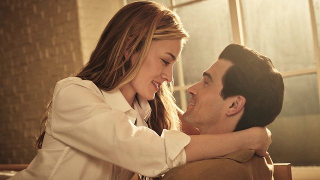 Sarah Pidgeon sitzt als Carolyn Besette auf dem Schoß von Paul Anthony Kelly als John F. Kennedy Jr. Sie hat ihre Arme um seinen Hals gelegt und die beiden schauen sich tief in die Augen.