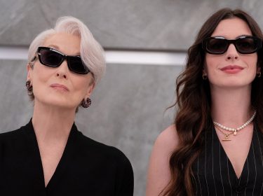Auf dem Bild zu Der Teufel trägt Prada 2 sind Miranda Priestly, gespielt von Meryl Streep, und Andrea Sachs, dargestellt von Anne Hathaway, nebeneinander zu sehen. Beide tragen dunkle Sonnenbrillen und elegante schwarze Outfits. Miranda wirkt kühl und autoritär, während Andrea selbstbewusst und stilvoll auftritt. Die Szene strahlt Macht, Modebewusstsein und eine spannungsgeladene Dynamik aus.