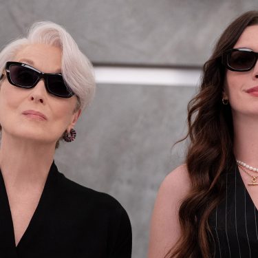 Auf dem Bild zu Der Teufel trägt Prada 2 sind Miranda Priestly, gespielt von Meryl Streep, und Andrea Sachs, dargestellt von Anne Hathaway, nebeneinander zu sehen. Beide tragen dunkle Sonnenbrillen und elegante schwarze Outfits. Miranda wirkt kühl und autoritär, während Andrea selbstbewusst und stilvoll auftritt. Die Szene strahlt Macht, Modebewusstsein und eine spannungsgeladene Dynamik aus.