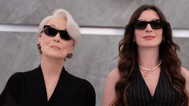 Auf dem Bild zu Der Teufel trägt Prada 2 sind Miranda Priestly, gespielt von Meryl Streep, und Andrea Sachs, dargestellt von Anne Hathaway, nebeneinander zu sehen. Beide tragen dunkle Sonnenbrillen und elegante schwarze Outfits. Miranda wirkt kühl und autoritär, während Andrea selbstbewusst und stilvoll auftritt. Die Szene strahlt Macht, Modebewusstsein und eine spannungsgeladene Dynamik aus.