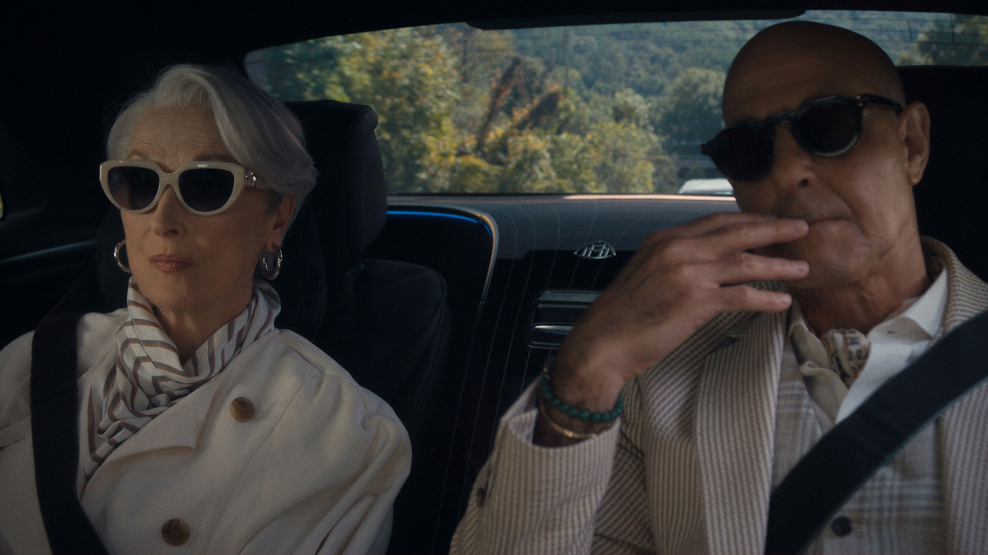 Auf dem Bild zu Der Teufel trägt Prada 2 sind Miranda Priestly, gespielt von Meryl Streep, und Nigel, dargestellt von Stanley Tucci, auf der Rückbank eines luxuriösen Autos zu sehen. Beide tragen elegante Outfits und dunkle Sonnenbrillen. Miranda sitzt ruhig und selbstbewusst links. Nigel wirkt konzentriert rechts neben ihr. Die Szene wirkt exklusiv und strahlt Macht sowie modische Autorität aus.