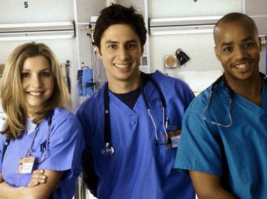 Auf dem Bild zu Scrubs beste Folgen sind drei Hauptcharaktere der Serie Scrubs in einem Krankenhaus zu sehen. Links steht Elliot, gespielt von Sarah Chalke, freundlich lächelnd in blauer OP-Kleidung. In der Mitte J.D., dargestellt von Zac Braff, locker und optimistisch. Rechts steht Turk, gespielt von Donald Faison, selbstbewusst und gut gelaunt.