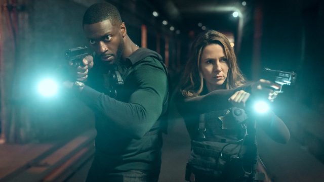 Aldis Hodge als Detective Alex Cross und Alona Tal als Special Agent Kayla Craig. Beide stehen mit gezogener Pistole und einer Taschenlampe im Dunkeln.