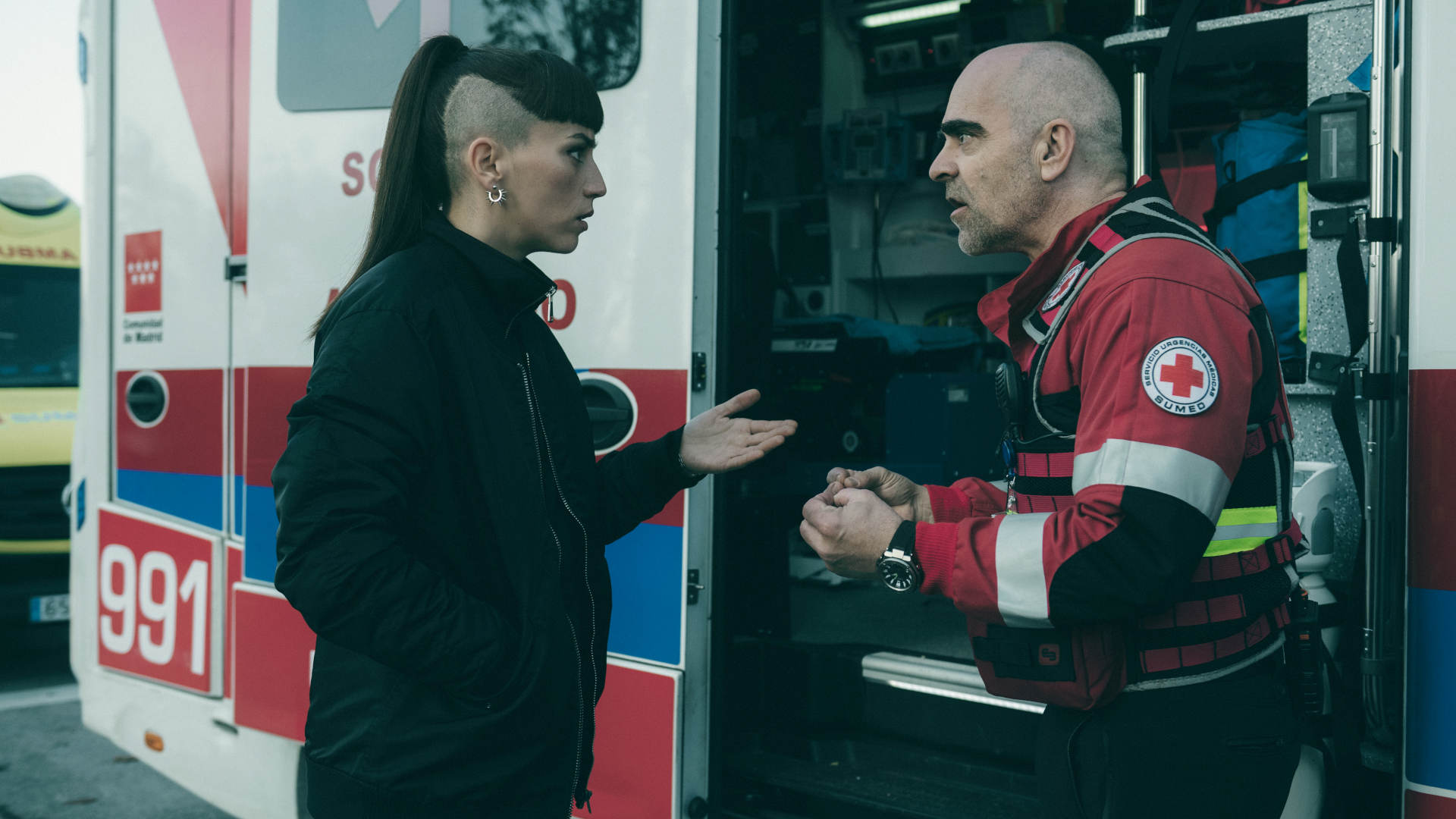 Julia und Salvador sprechen vor einem Rettungswagen miteinander.