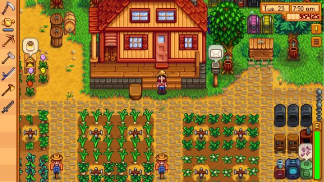 Auf dem Bild aus dem Videospiel Stardew Valley ist der Spieler-Charakter mit Strohhut, rotem Hemd und blauer Latzhose vor einem gemütlichen Farmhaus mit rotem Dach zu sehen. Gepflegte Felder mit Mais und grünen Pflanzen umgeben das Haus, während Maschinen und Kisten rechts platziert sind.