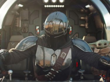 Der Mandalorianer Din Djarin und sein Schüler Grogu sitzen im Cockpit eines futuristischen Fahrzeuges.