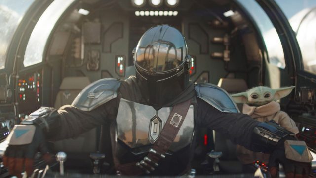 Der Mandalorianer Din Djarin und sein Schüler Grogu sitzen im Cockpit eines futuristischen Fahrzeuges.