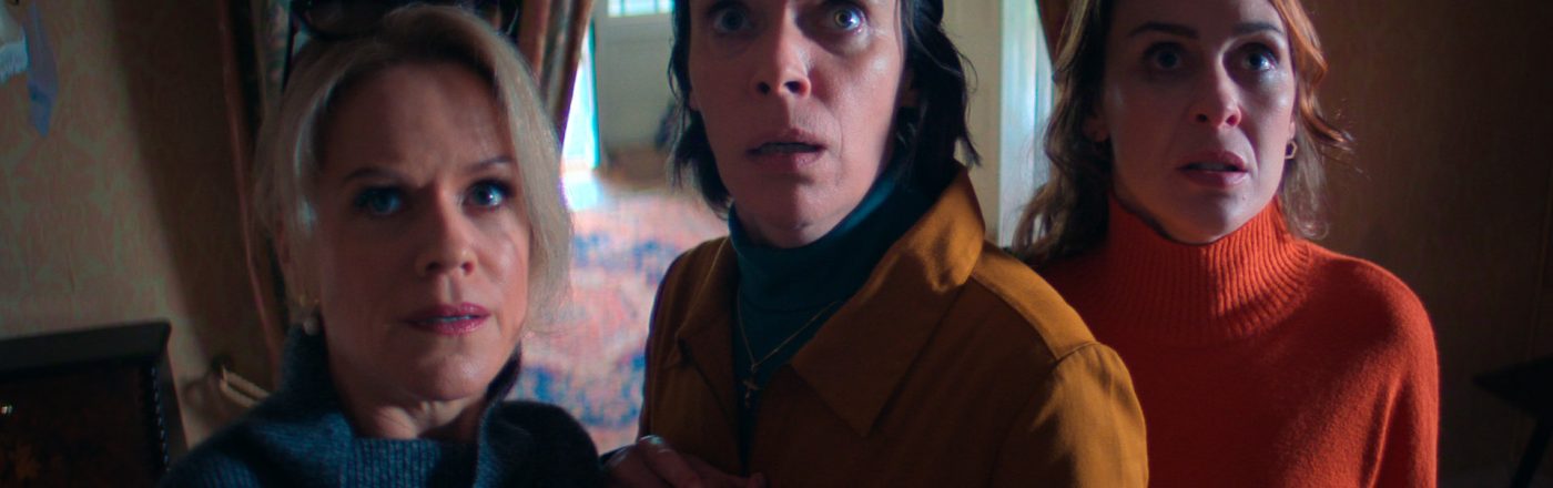 Szenenbild aus Hot To Get To Heaven From Belfast: Drei Frauen stehen mit schockiertem Blick in einer dramatischen Szene in einem Wohnzimmer vor einem Vorhang.